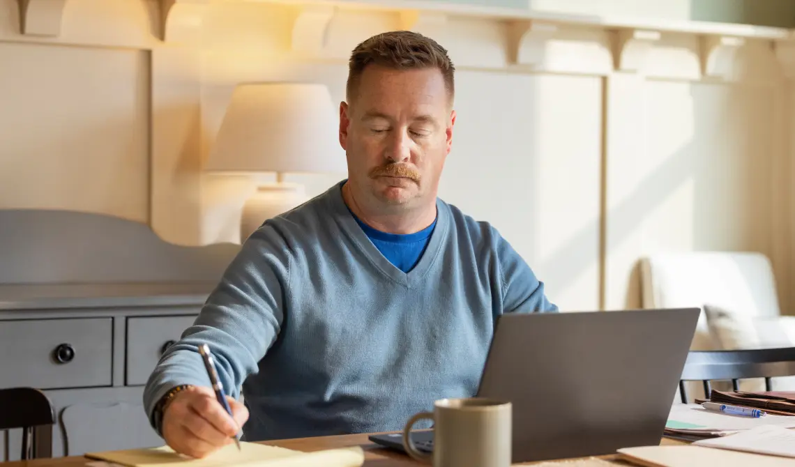 middle-aged male subject taking notes in front of a laptop