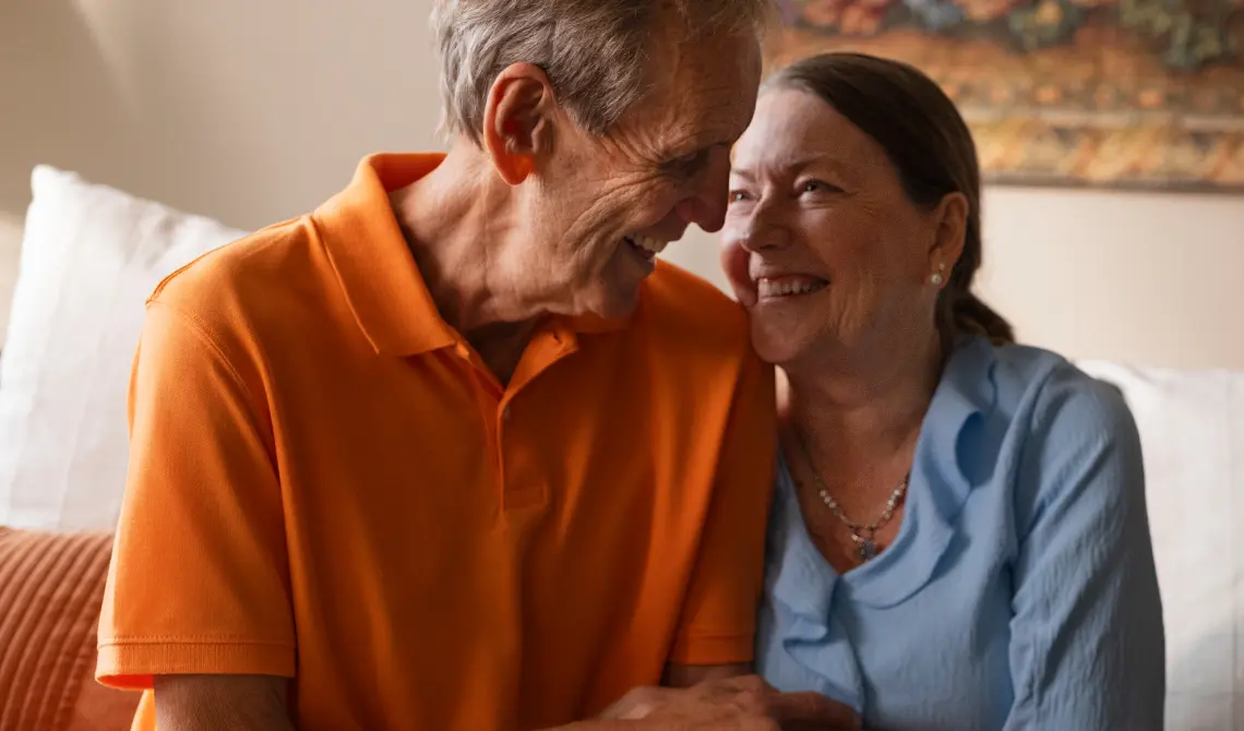 senior couple sitting together in their home smiling at each other