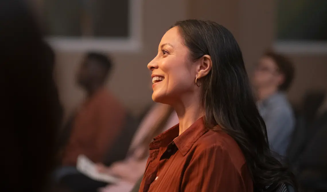 woman smiling brightly as she sits in an engaged crowd of people