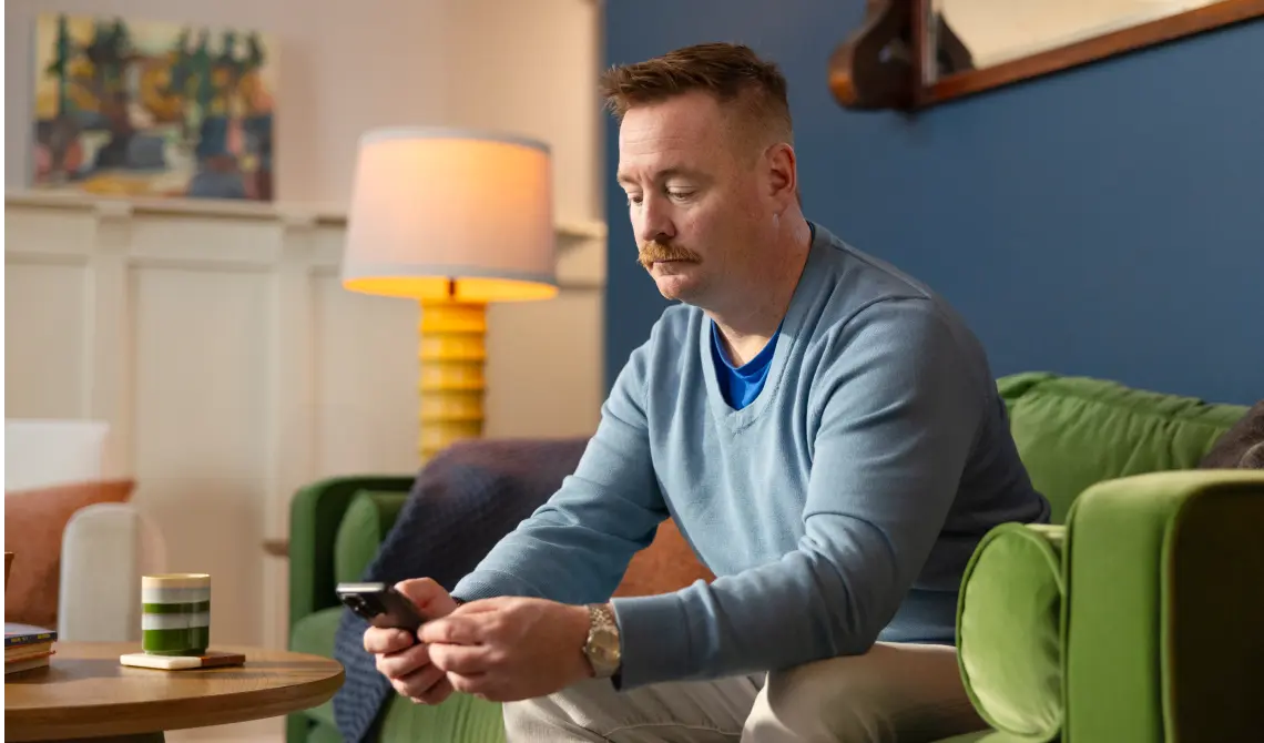 Middle aged man looking at phone on couch